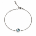 A delicate silver chain finish bracelet with a single bezel-set light blue gemstone, displayed on a clean, light pink background.